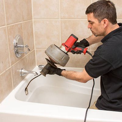 Plumber unclogging a tub drain with an electric auger.